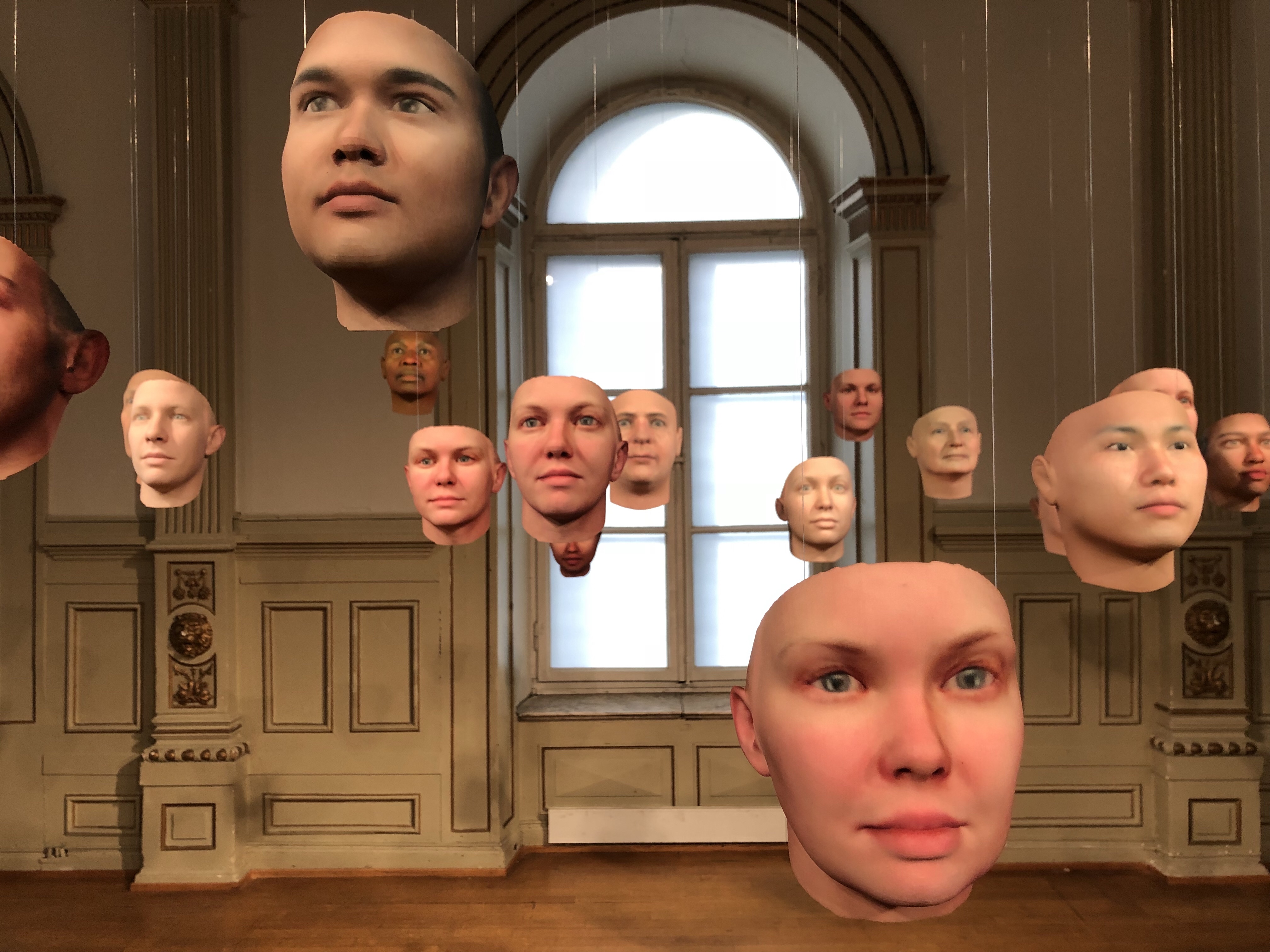 Many masks resembling human faces hang from the ceiling in an art gallery.