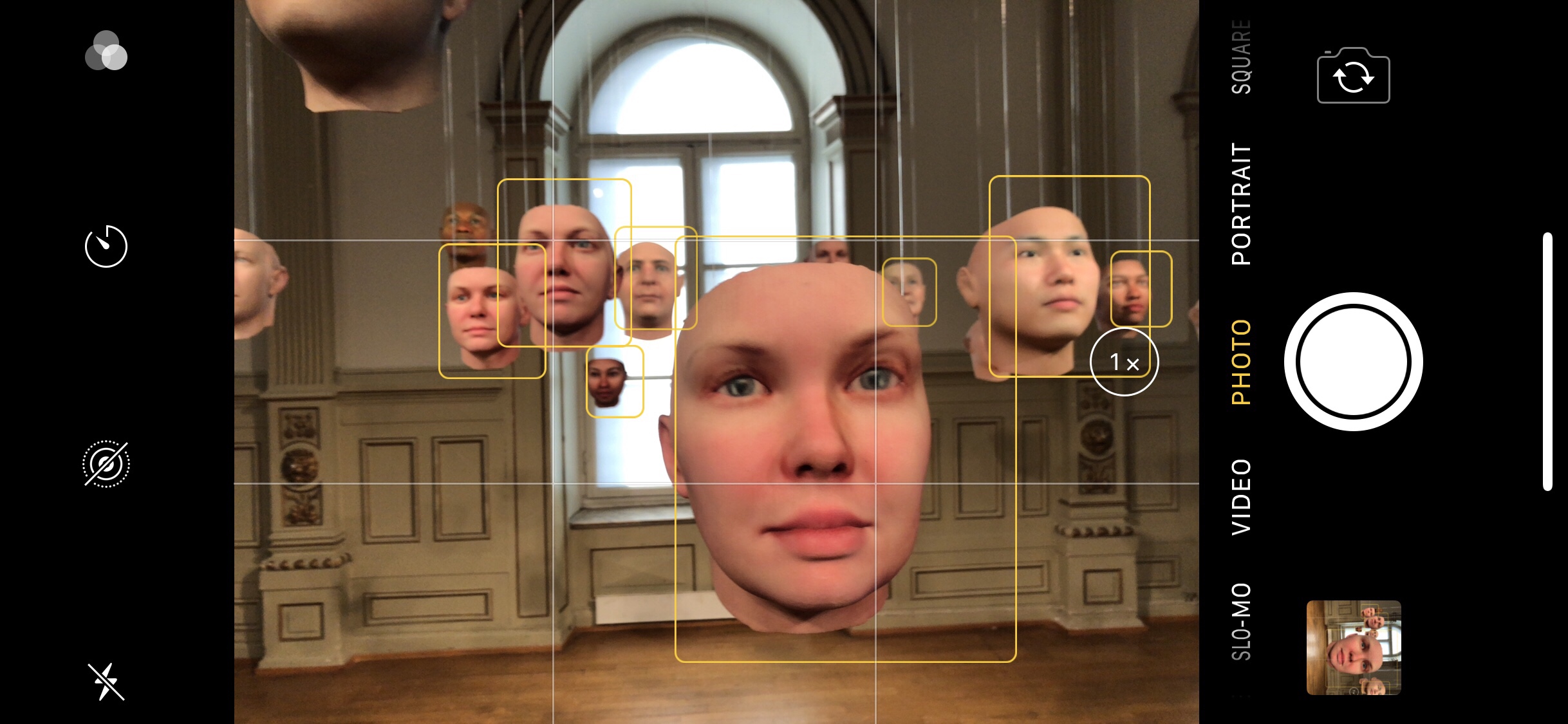 A screenshot of the iPhone camera interface showing hanging masks resembling human faces in an art gallery, and yellow squares around each mask indicating that the phone camera has recognised a human face.